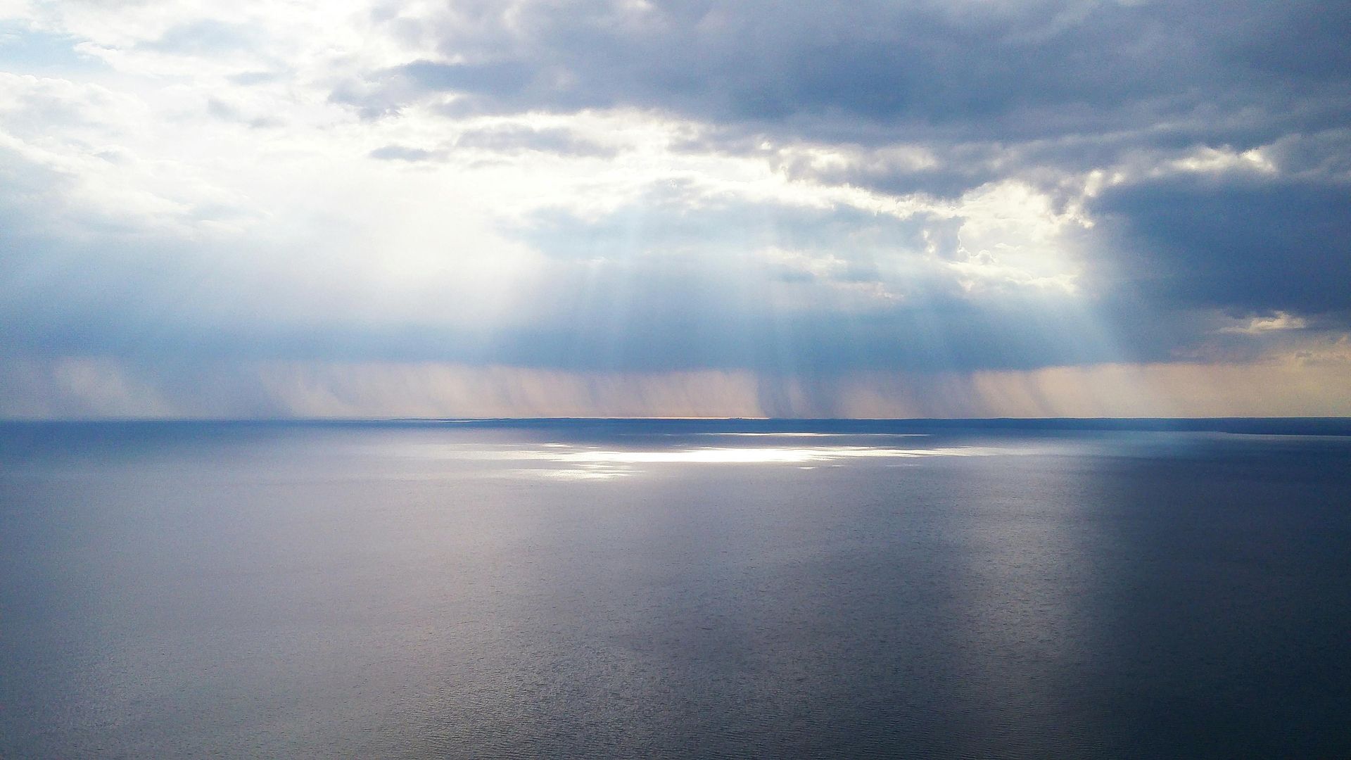 Sunlight breaking through clouds over a calm body of water.