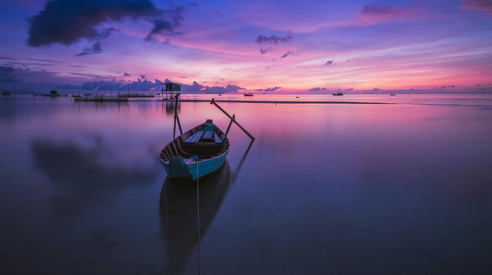 A small boat in calm water, reflecting a purple and pink sunset.