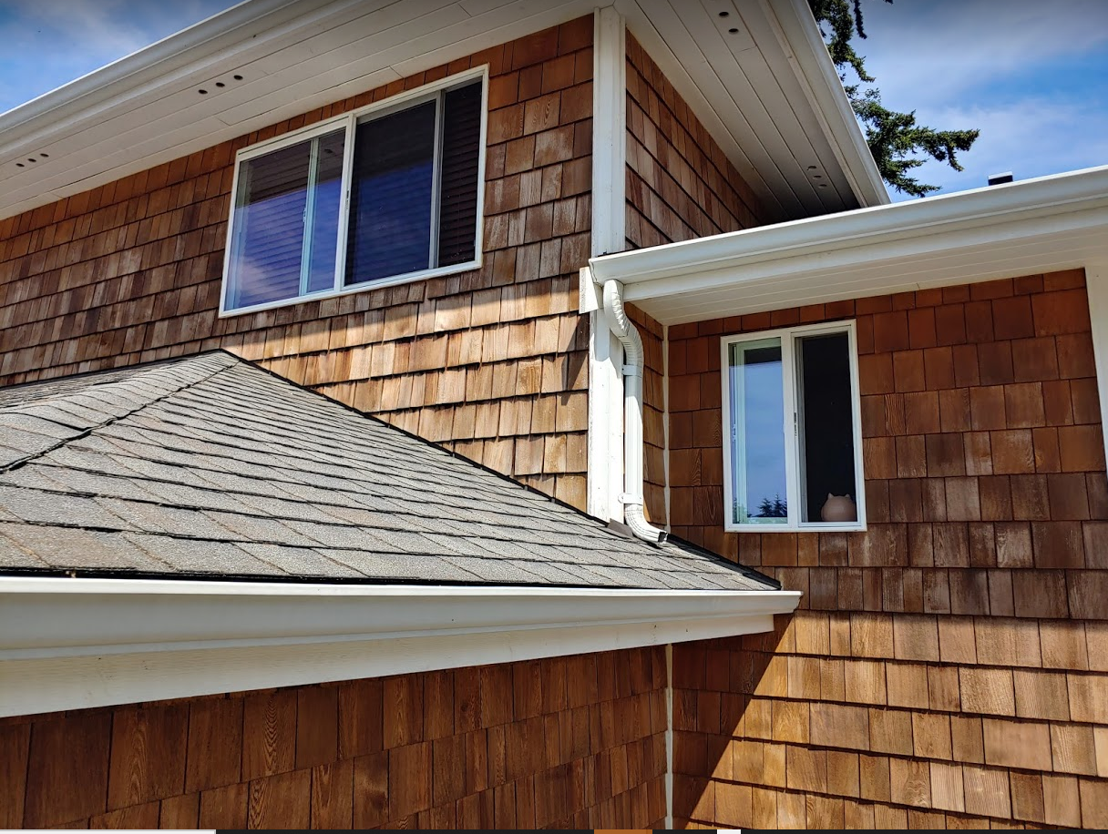 Freshly cleaned Cedar wood-sided house with shingle roof, white trim, and two windows.
