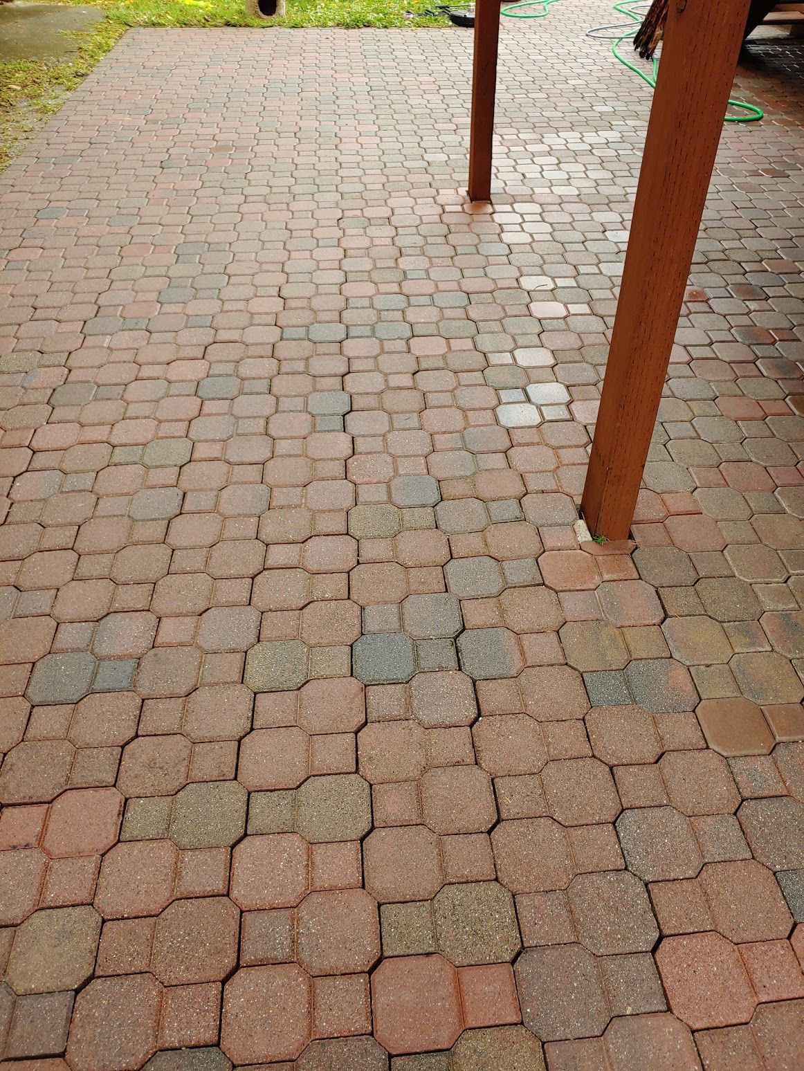 Freshly cleaned brick patio with square and octagonal pavers, brown support posts, and green grass in the background.