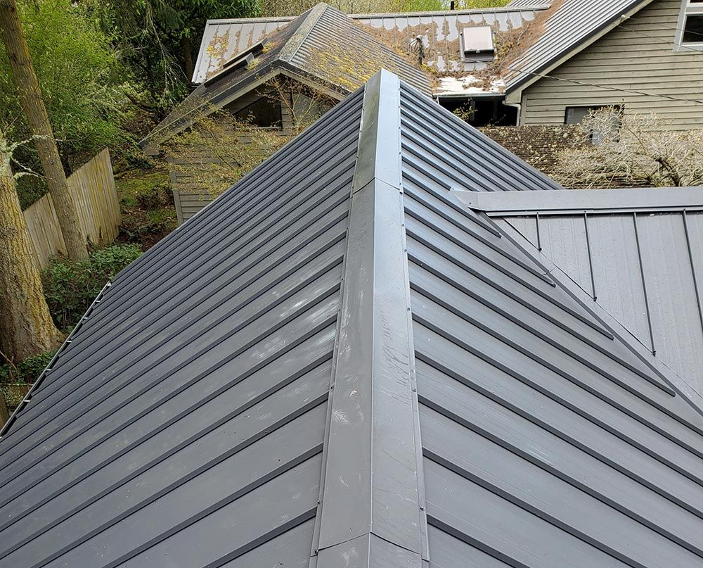 Freshly cleaned gray metal roof with a central ridge, viewed from above, with other buildings in the background.