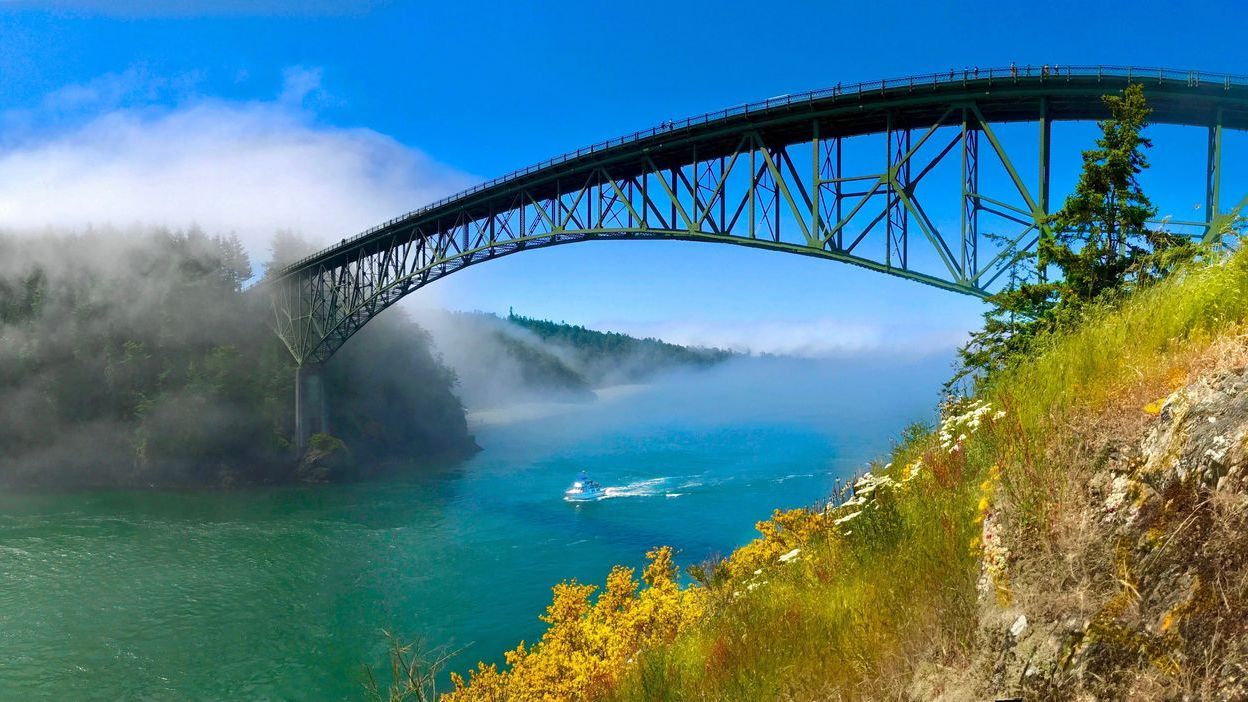 Steel arch bridge over turquoise water, with fog and lush greenery.