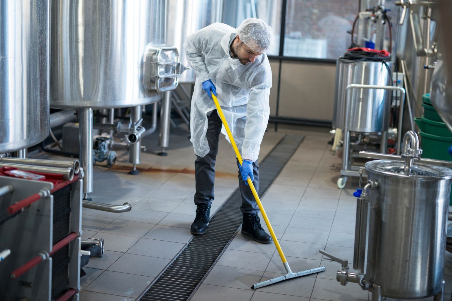 Worker cleaning industrial floor with a mop in a stainless steel production area