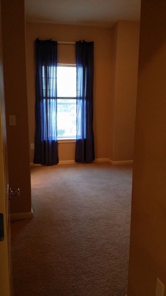 An empty bedroom with a window and blue curtains.