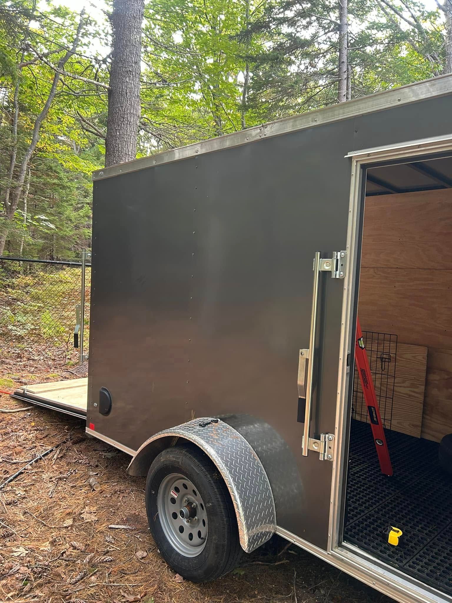 Dark gray cargo trailer with open door in wooded setting.