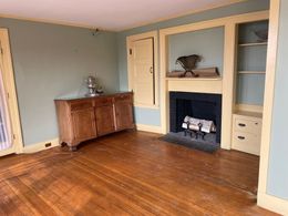 Empty room with hardwood floors, fireplace, built-in shelves, and a wooden cabinet.