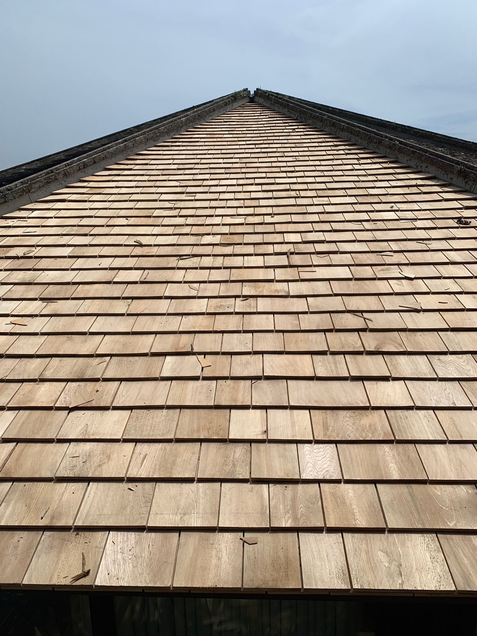 View of a wooden shingled roof reaching upwards; sky in the background.