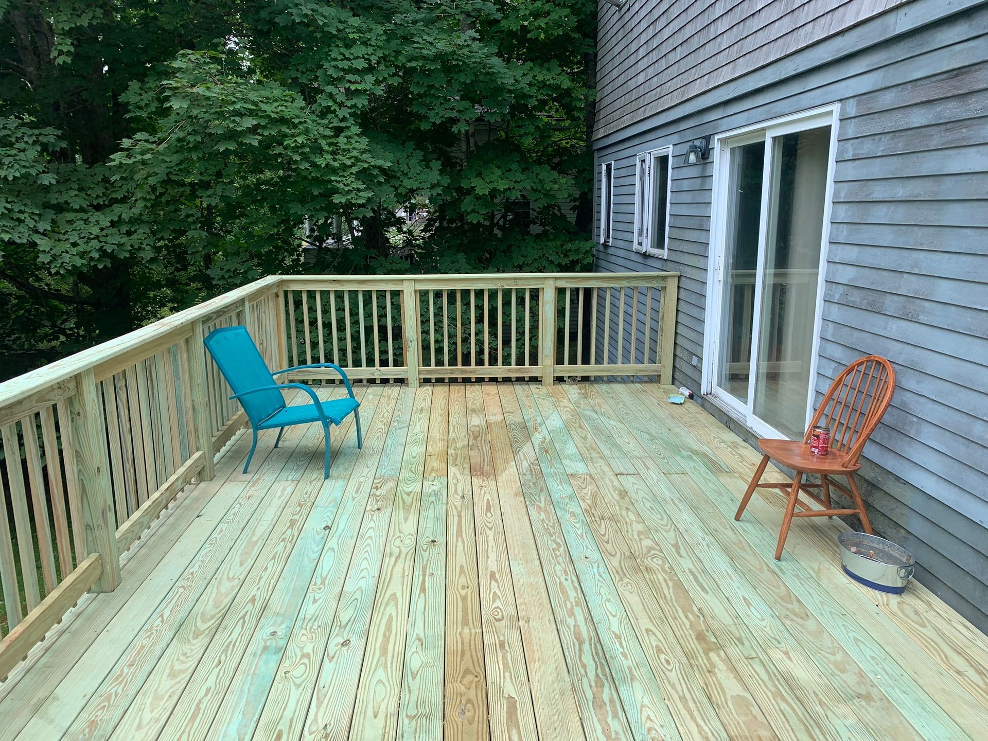 Wooden deck with two chairs, next to a house, and surrounded by trees.