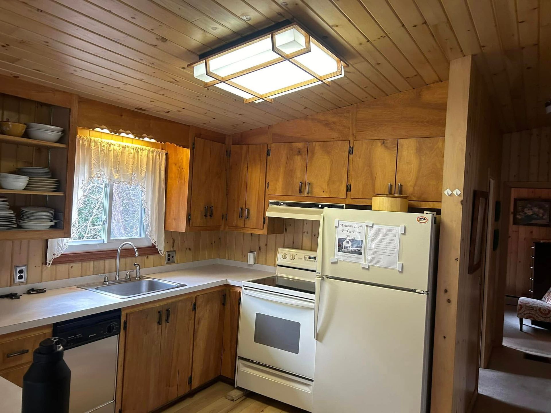 Small rustic kitchen with wooden cabinets, a white fridge, and a window with a curtain.