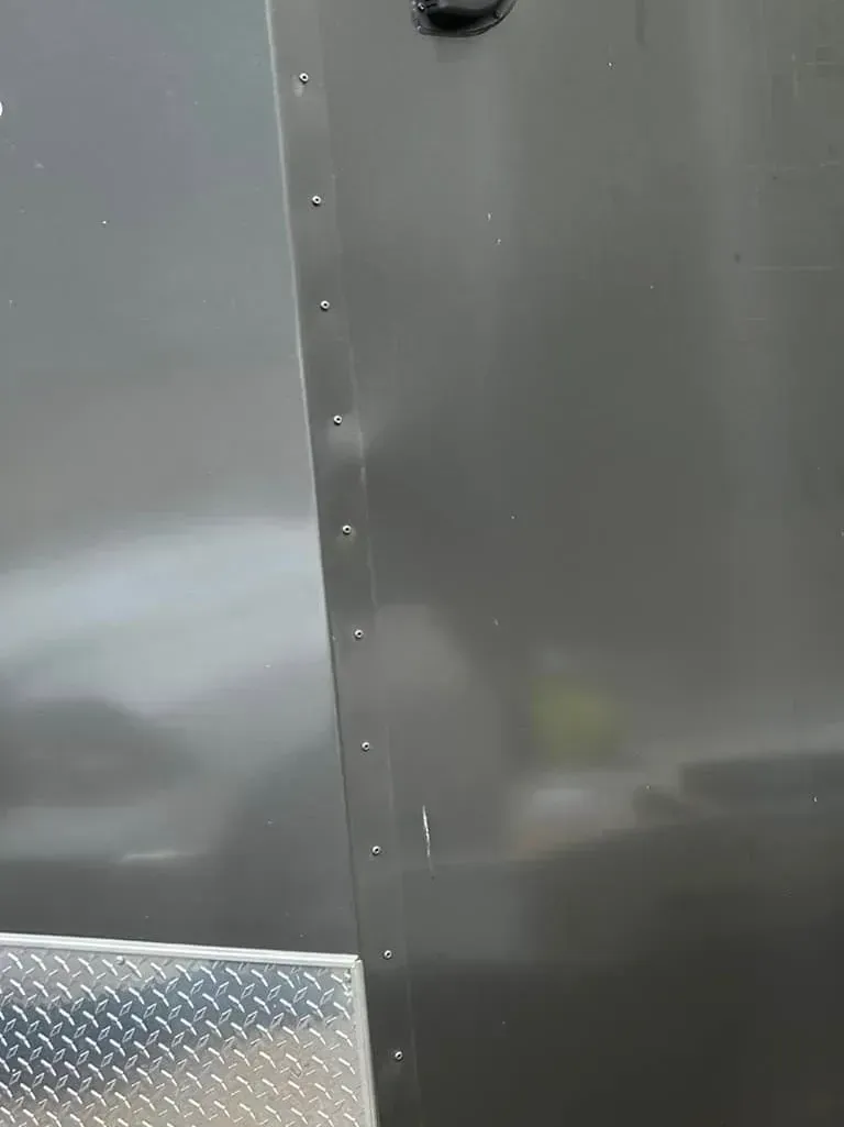 Close-up of a dark metal surface joined by rivets, with a diamond-plate metal edge at the bottom.