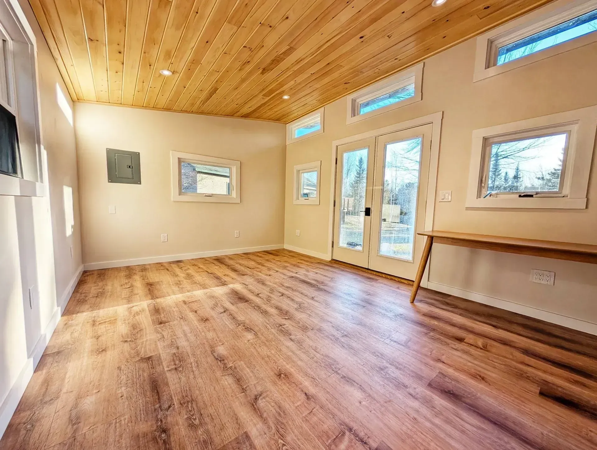 Interior of a small room with wood flooring, light walls, a wood ceiling, and French doors.
