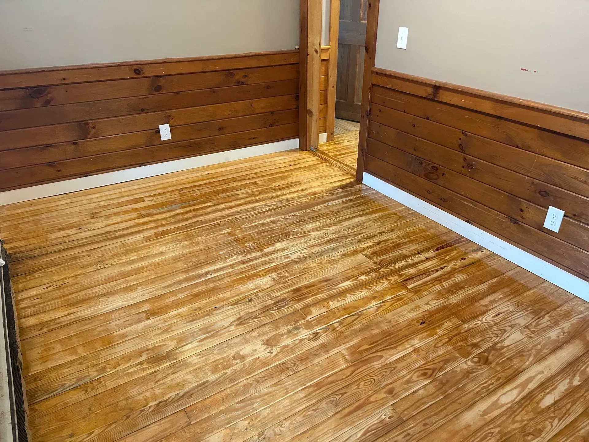 Empty room with wood-paneled walls, wooden floor, and an open doorway.