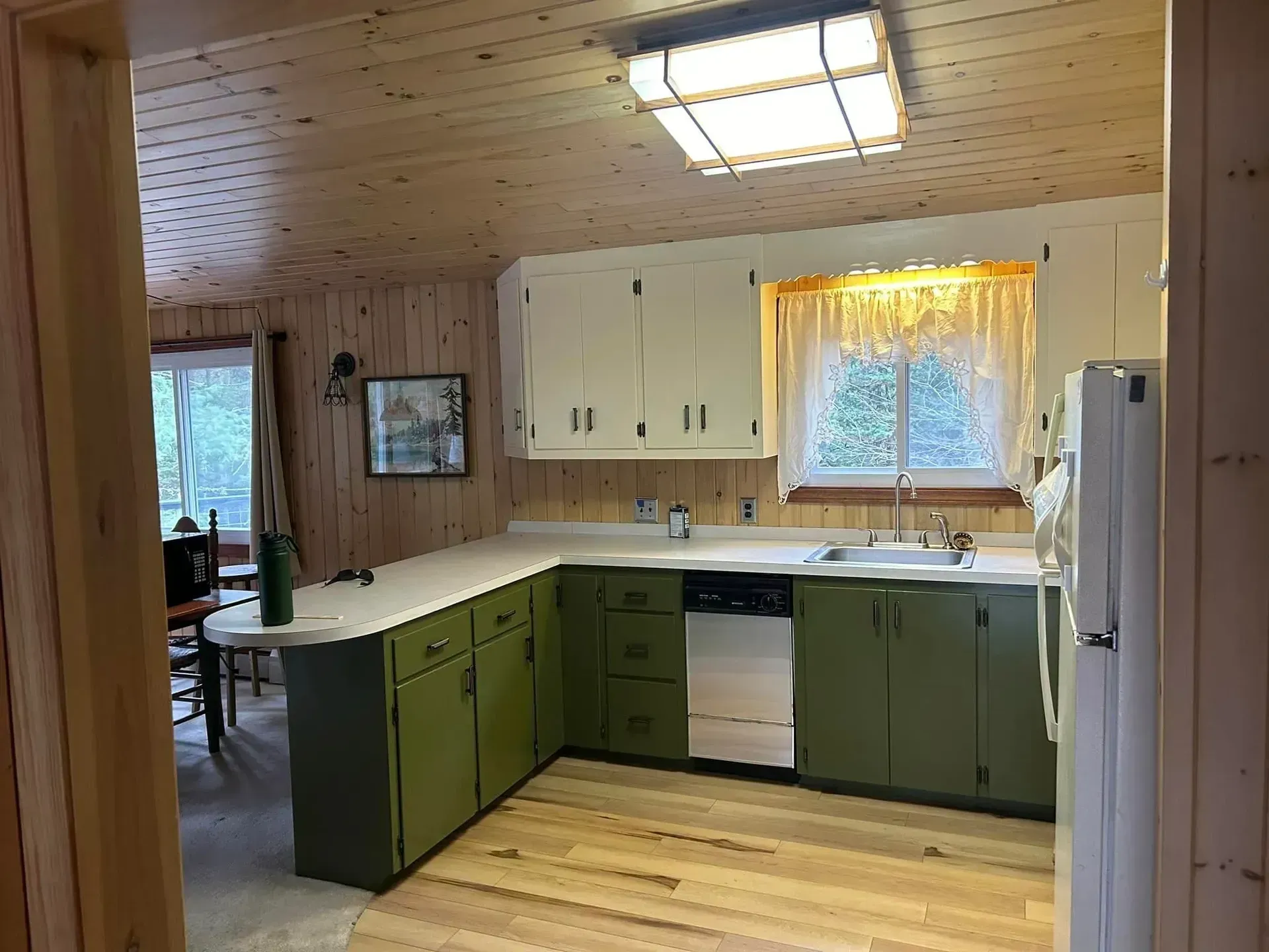 Kitchen with green cabinets, white countertops, and wood paneling.