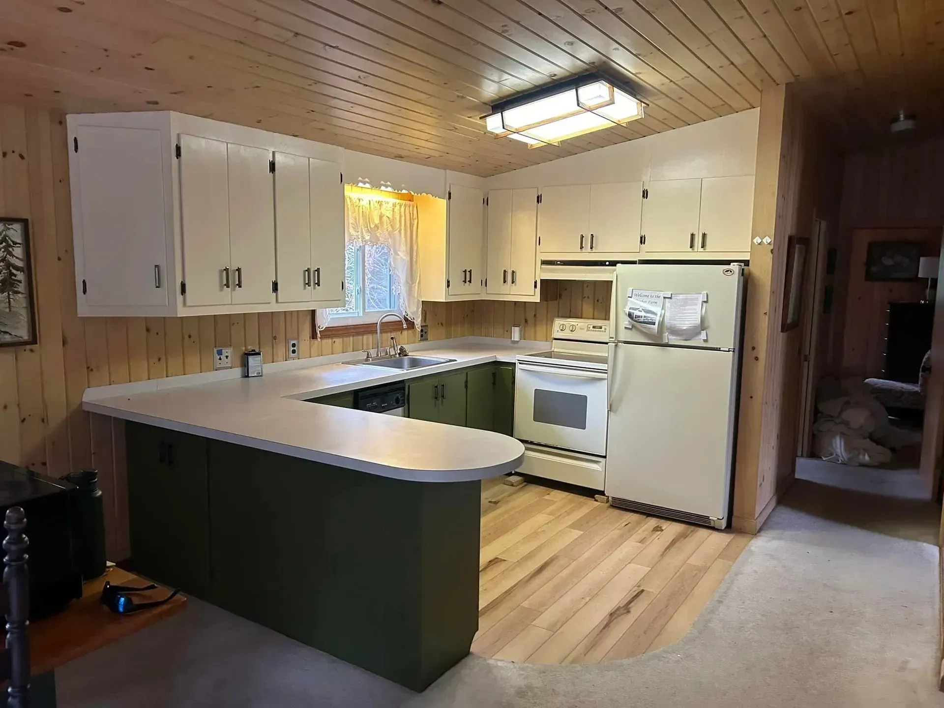 Kitchen with light wood floors, white appliances, olive green cabinets, and a light-colored countertop.