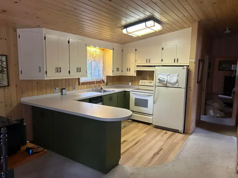 Kitchen with white cabinets, green accents, and a white refrigerator; wood walls and floor.