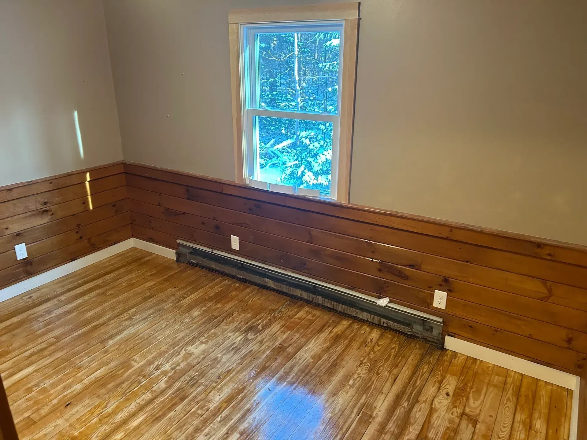 Empty room with wood paneling, hardwood floors, a window, and baseboard heater.
