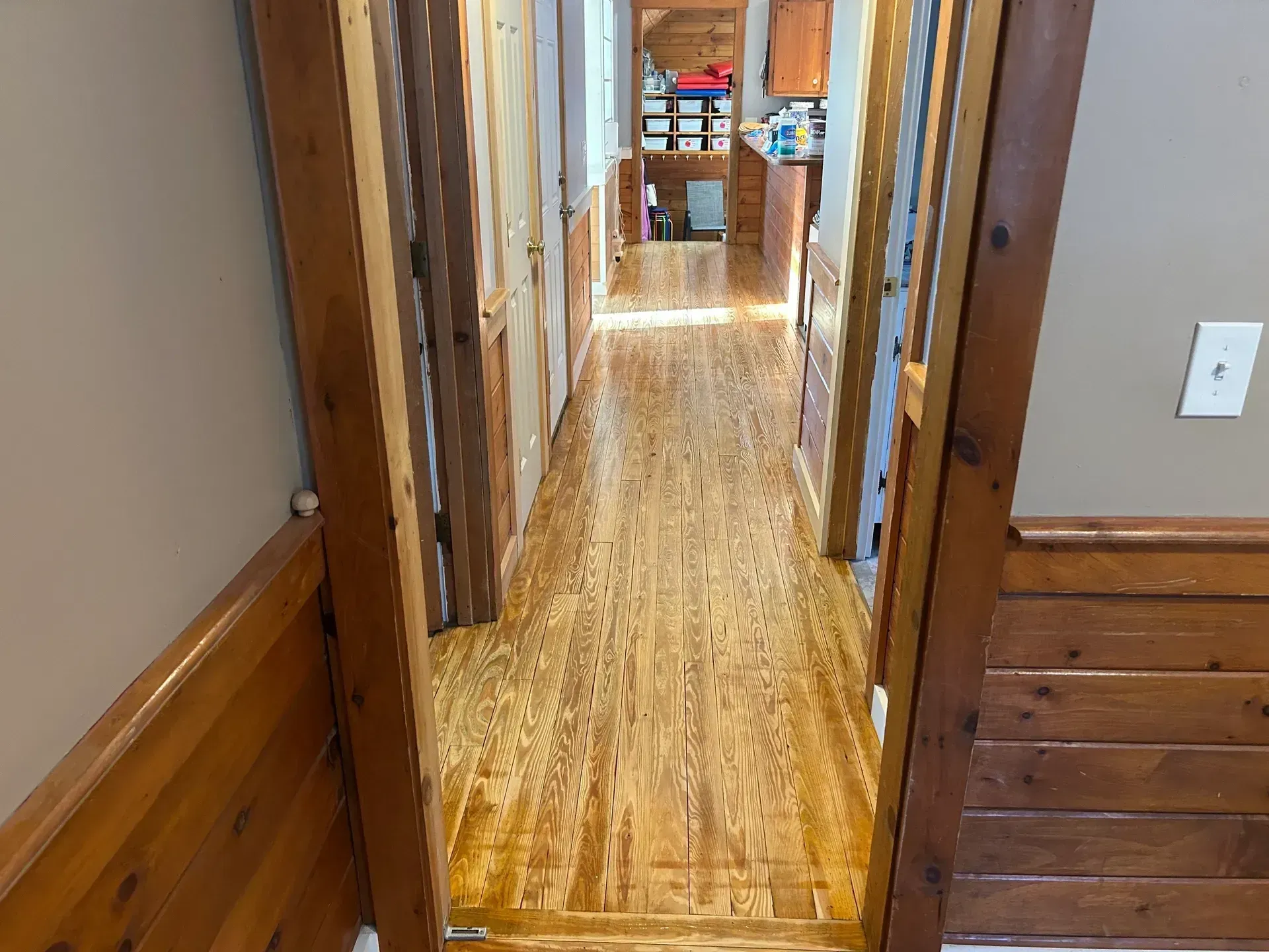 A hallway with wood flooring and paneling, with a doorway on the right.