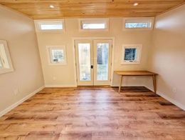 Empty room with wood floor and ceiling, light walls, French doors, windows, and a desk.