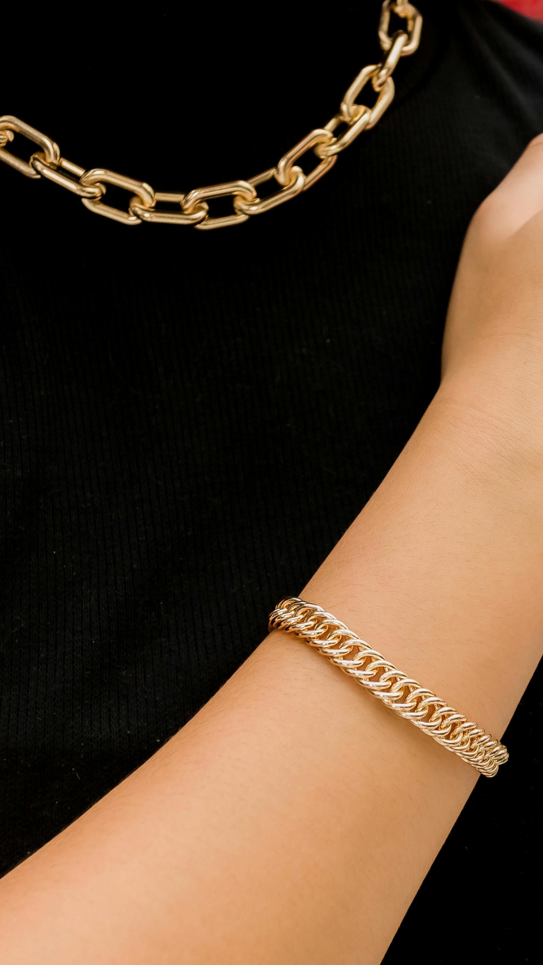 Gold chain necklace and bracelet on a person wearing a black shirt.