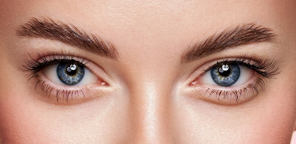 Close-up of a person's eyes, featuring blue irises, thick eyebrows, and visible eyelashes.