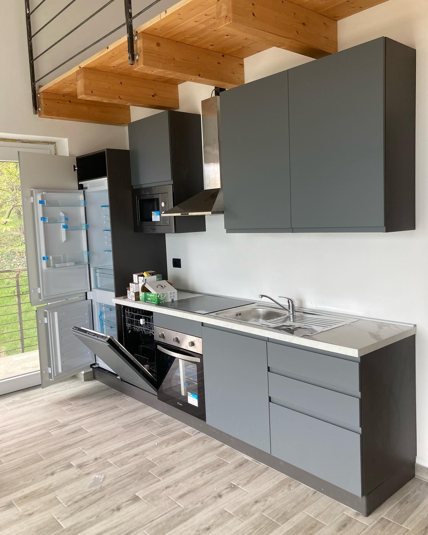 Una cucina con mobili grigi, un lavello, un forno e un frigorifero.