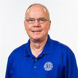 Man with glasses smiles, wearing blue polo shirt with logo in front of a white background.
