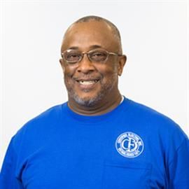 Man with glasses smiling, wearing a blue shirt with a logo, against a white background.