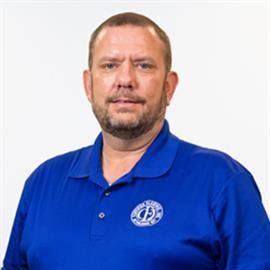 Man in a blue polo shirt with a logo, facing the camera, on a white background.
