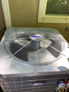 A Carrier air conditioner unit with a fan and gauges, set outdoors near a window.