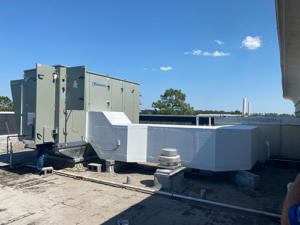 HVAC unit on a flat rooftop against a clear blue sky. White wrapped ductwork extends to the right.