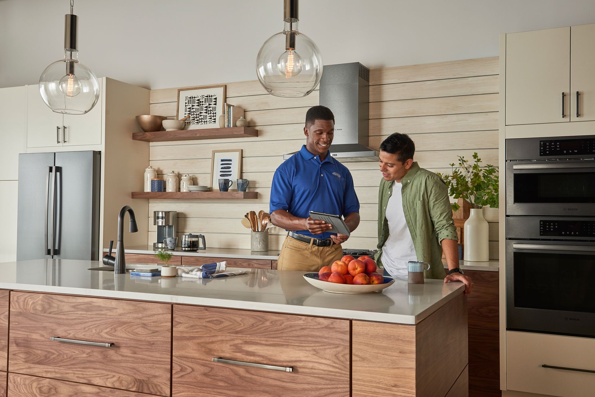 Two men in a modern kitchen, one in a blue shirt holding papers. Discussing in front of a counter.