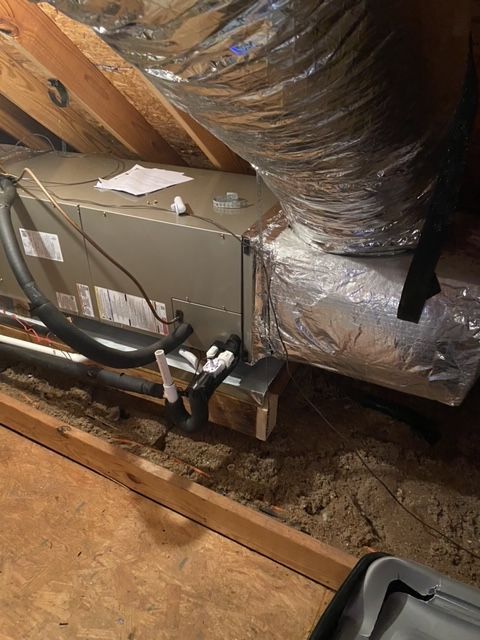 HVAC unit in an attic with ductwork, piping, and insulation.