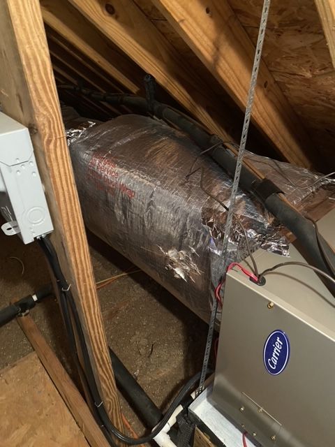 HVAC unit and ductwork in an attic, with reflective insulation and wooden beams.