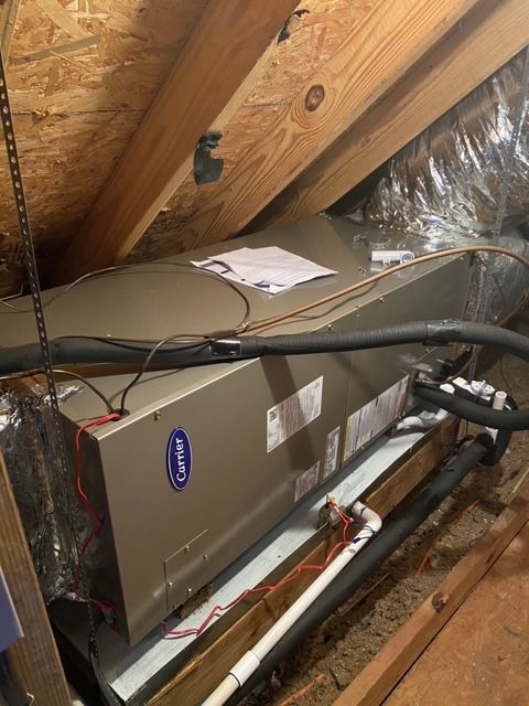 HVAC unit in an attic, with Carrier logo. Ductwork, pipes, and wooden beams are visible.
