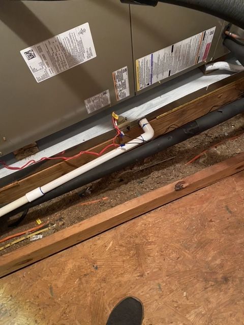 HVAC unit with exposed piping and wiring. Insulation and wooden framing visible in a crawl space.