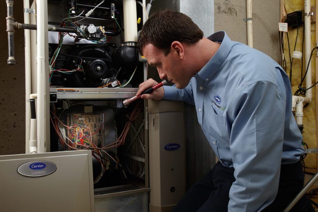HVAC technician examining a furnace's interior with a flashlight in a utility room.