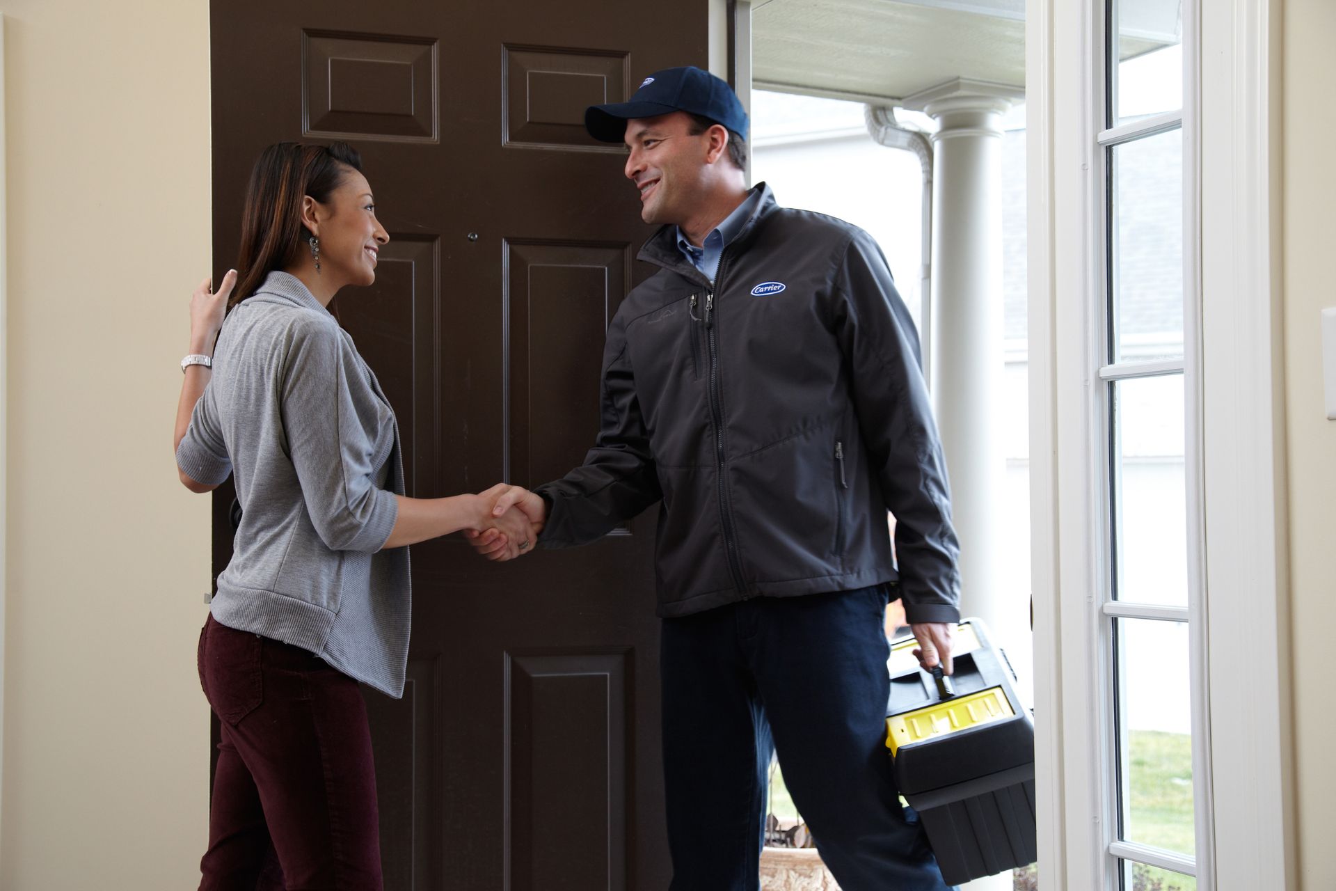 Woman shakes hands with service technician at a doorway, holding a toolbox.