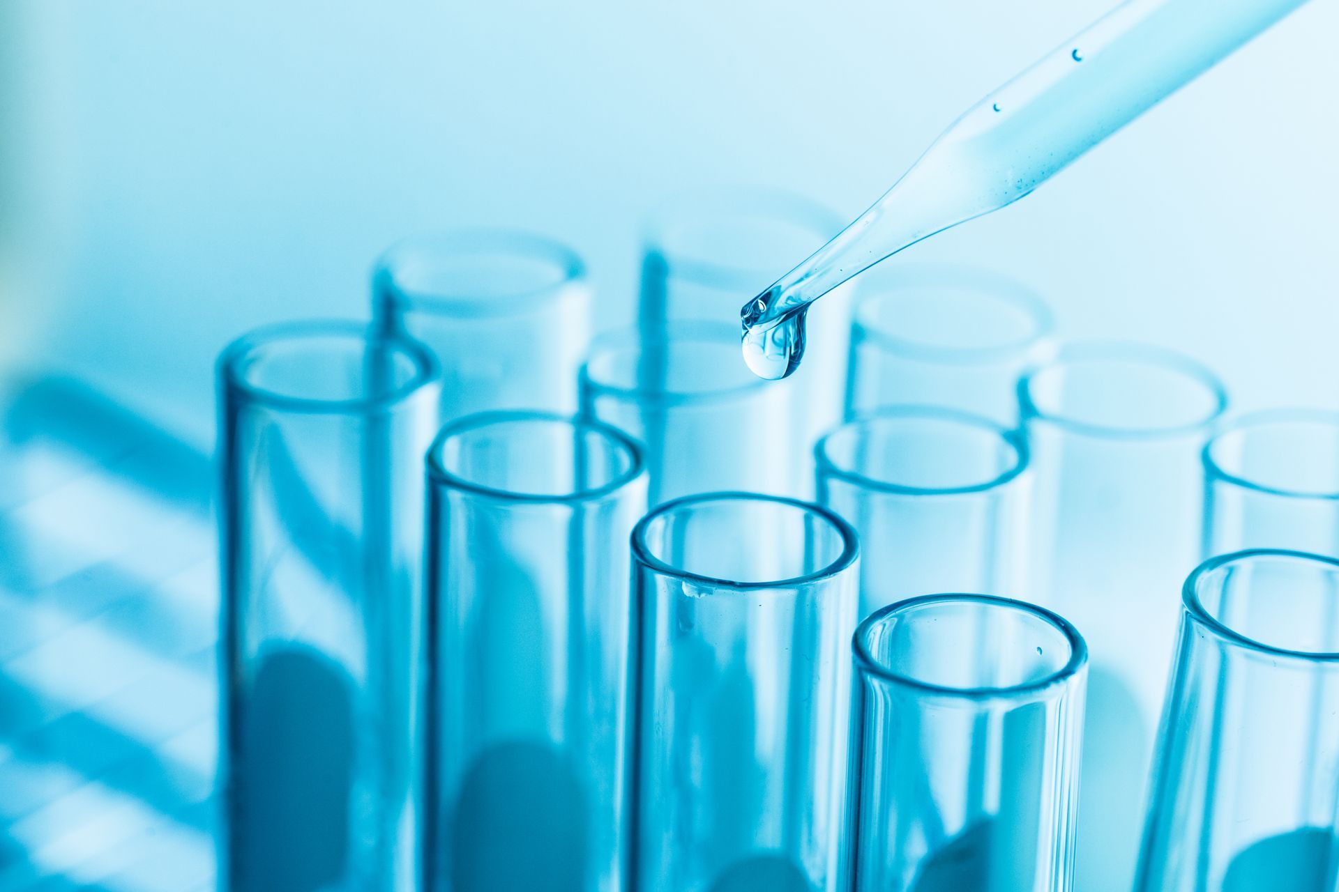 Test tubes with a pipette dropping liquid, blue-toned, laboratory setting.
