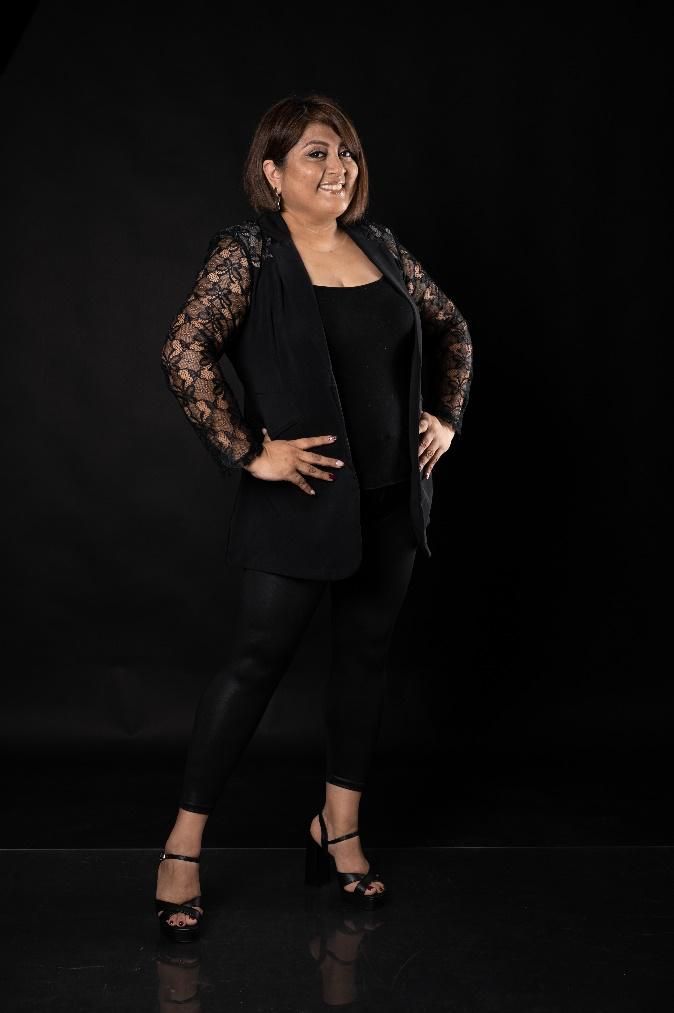 Una mujer con una chaqueta negra y pantalones negros está parada frente a un fondo negro.