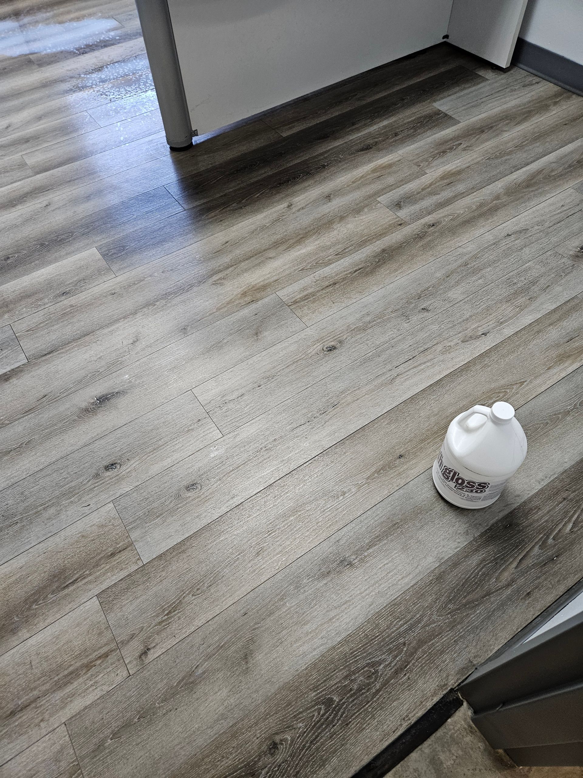 A gallon of milk is sitting on a wooden floor.