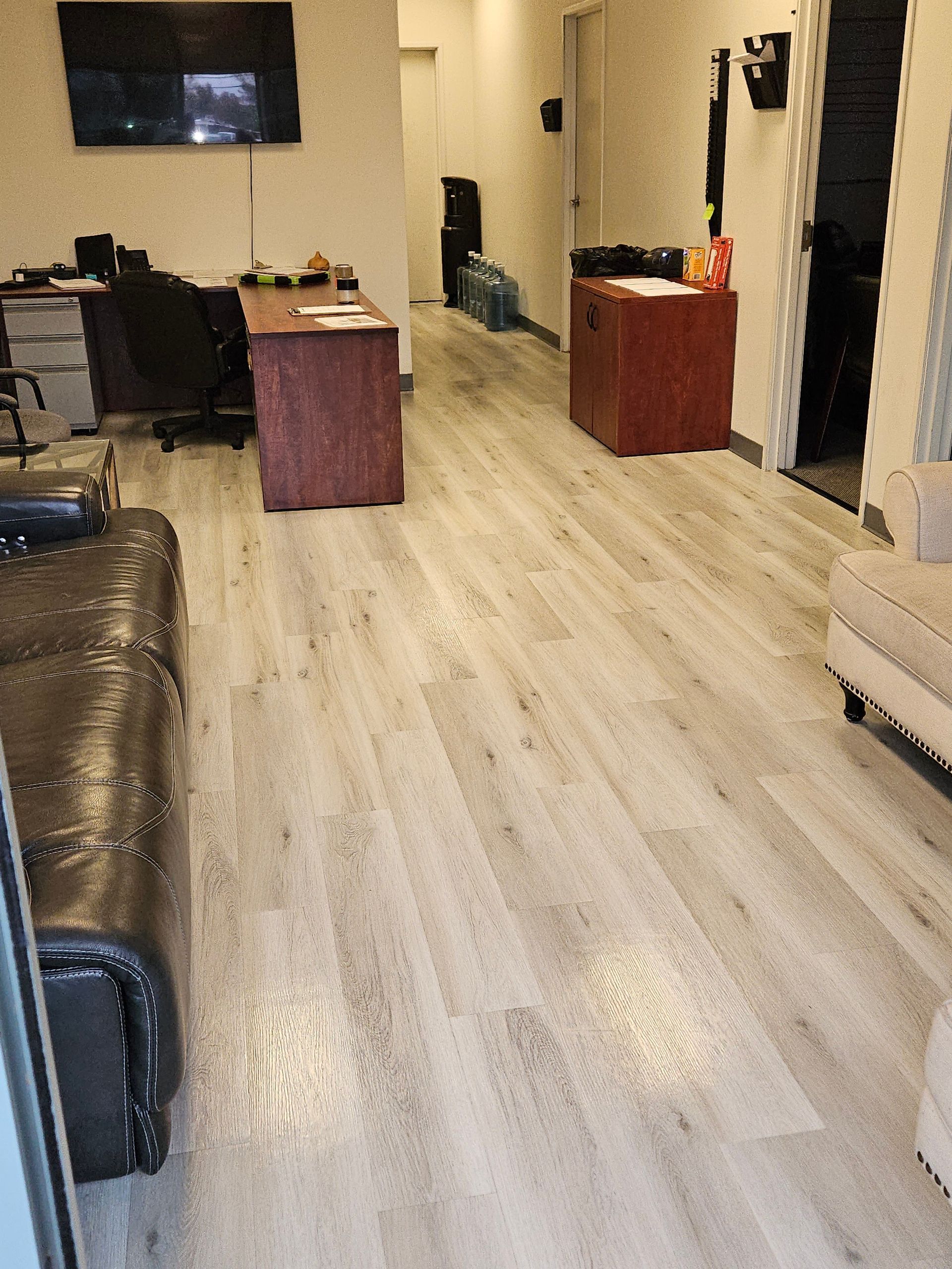 A living room with hardwood floors , a couch , a desk and a television.