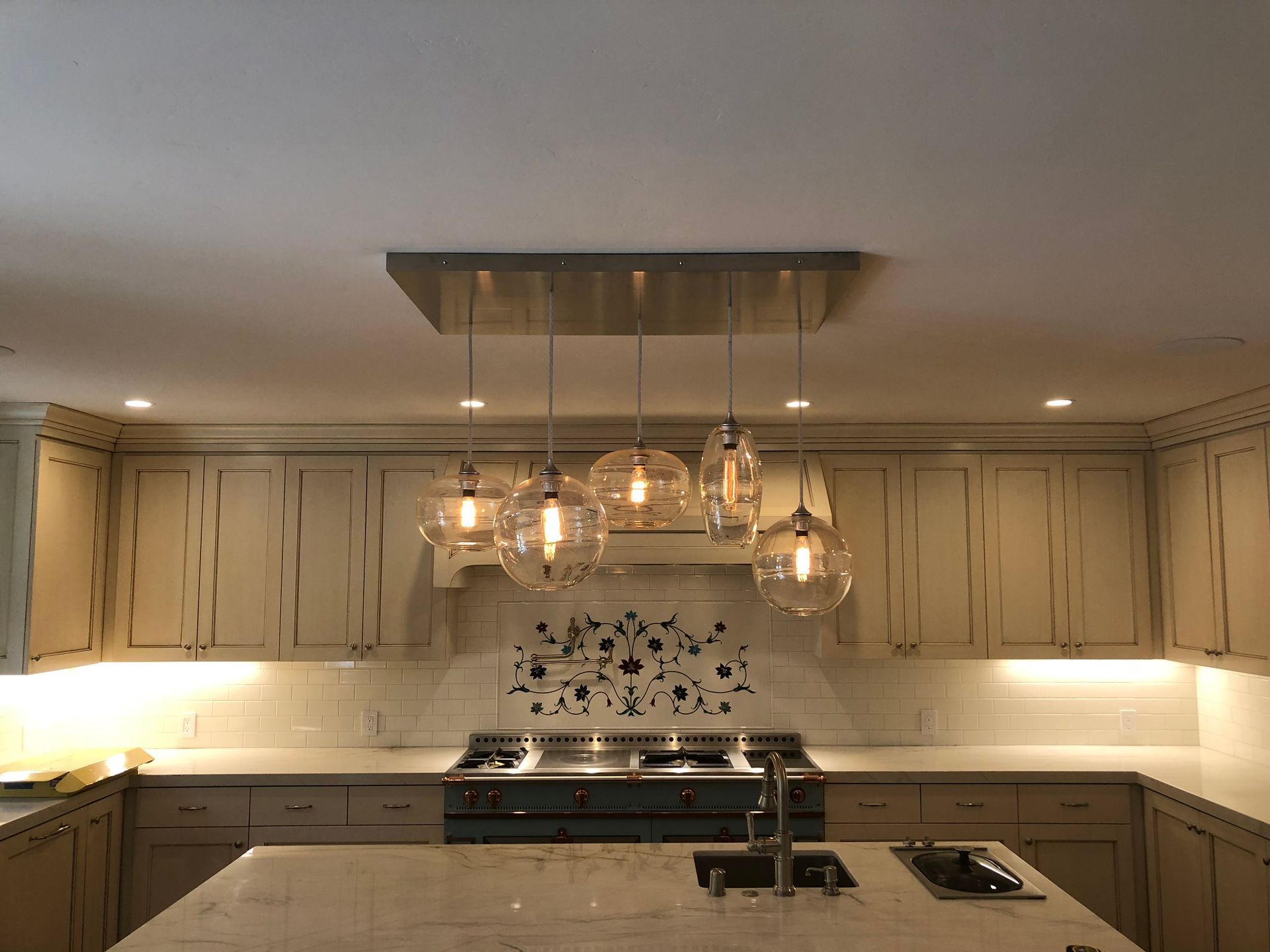 A kitchen with off-white cabinets, a central island, and a modern light fixture with glass globes hanging over the stove.