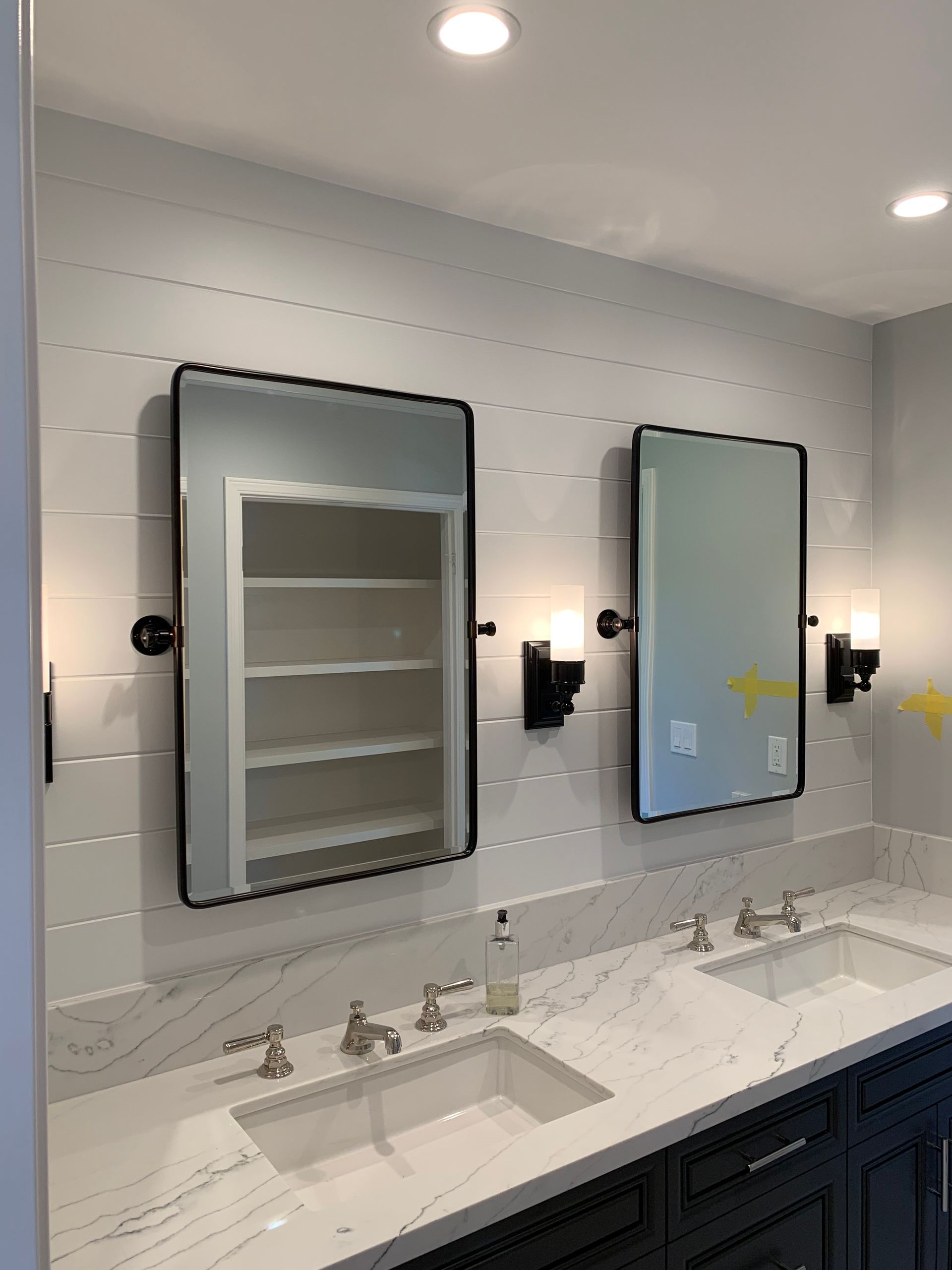 A modern bathroom with two sinks, large framed mirrors, and sconce lighting. The wall is white shiplap.