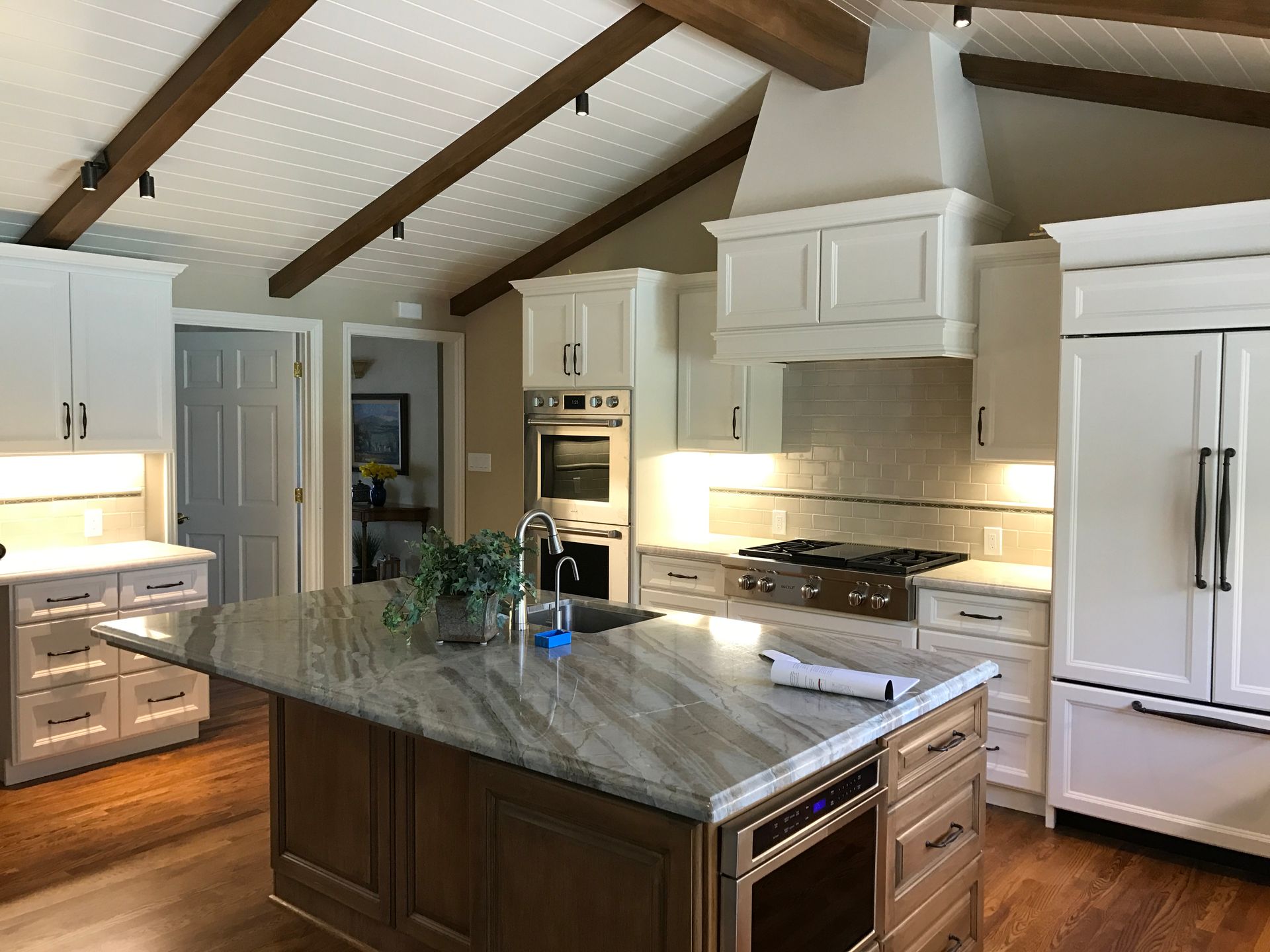 Spacious kitchen with a large island, white cabinets, stainless steel appliances, and exposed wooden beams on the ceiling.