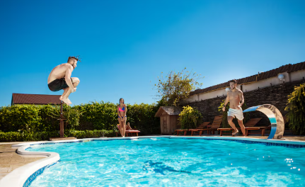 Gente saltando a una piscina azul en un día soleado.