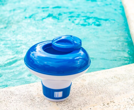 Clorador de piscina flotante azul y blanco en el borde de una piscina con agua azul.