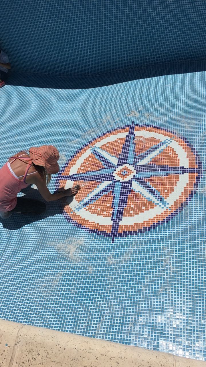 Niño en una piscina tocando un mosaico de brújula en el suelo.