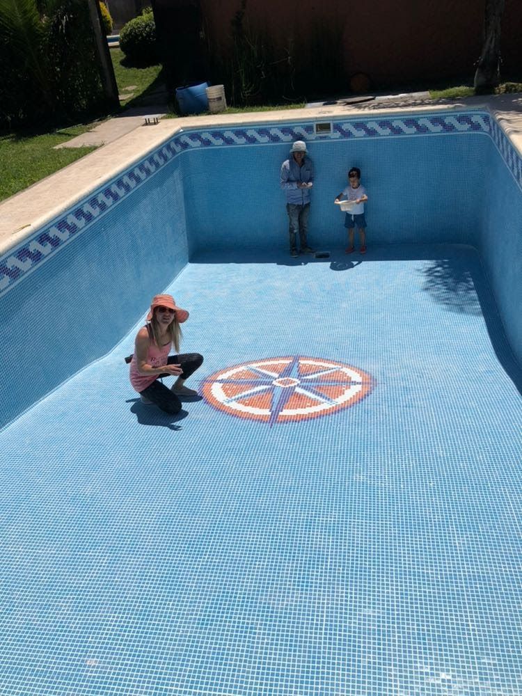 Personas en una piscina de mosaicos; una en cuclillas, dos de pie. El dibujo de una brújula se ve en el fondo de la piscina.