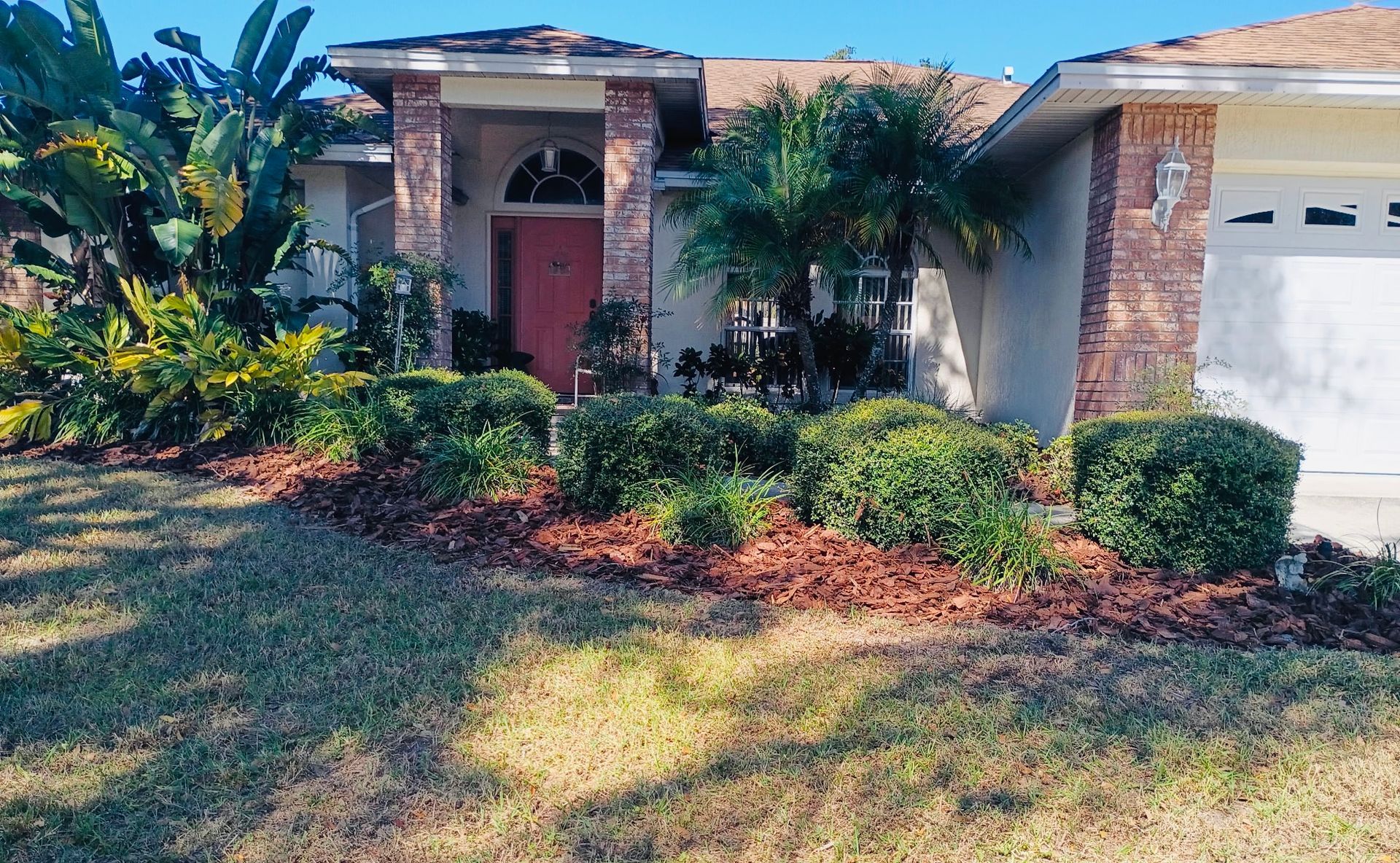 Suburban house with landscaped yard, including bushes, mulch, and a front door.