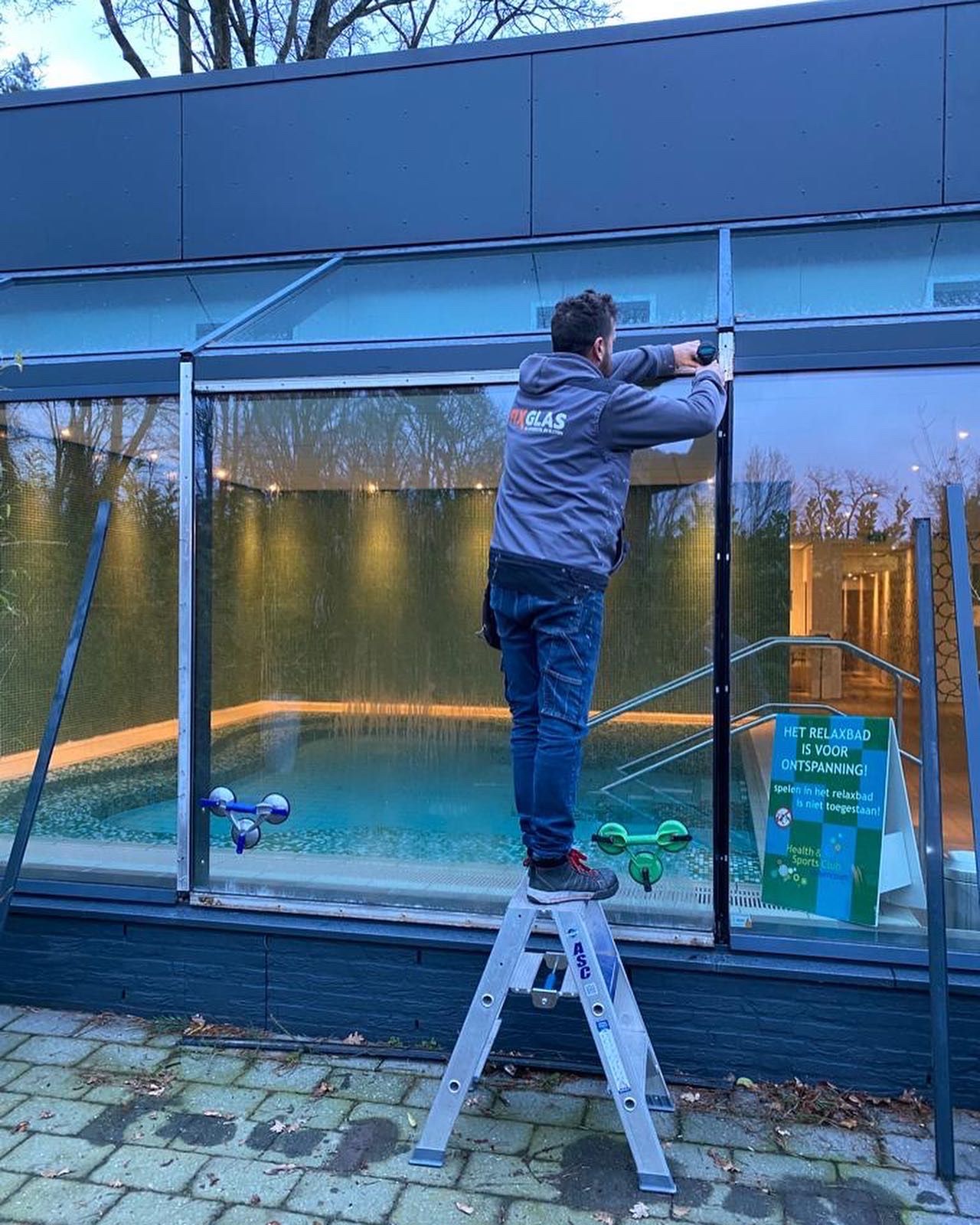 Een man staat op een ladder voor een zwembad.